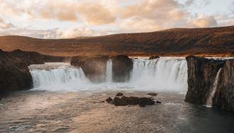 Trio of waterfalls cascading into river by bed of autumn covered land  