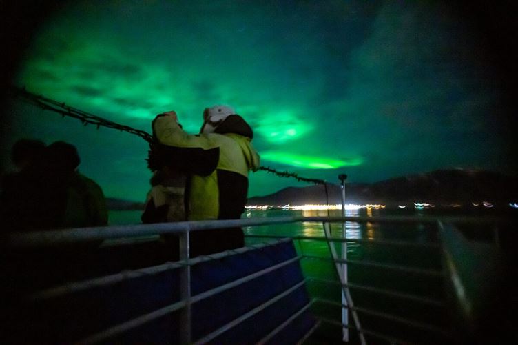 Tourist on Northern lights boat tour standing on edge of boat viewing the sky 