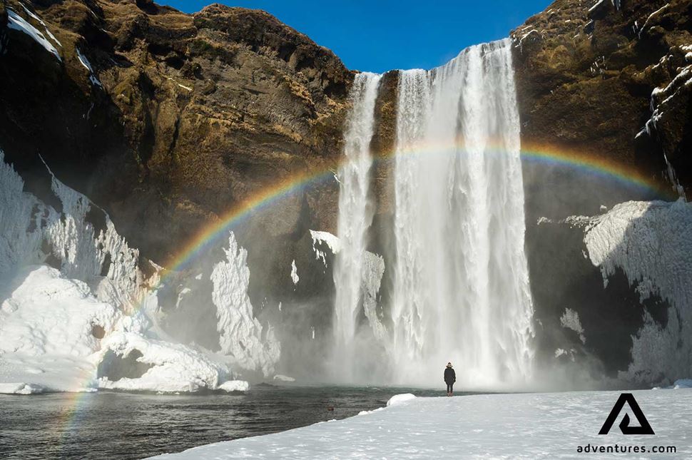 standing near skogafoss with a rainbow in winter 