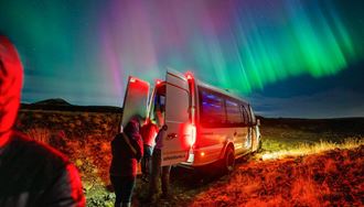 Tourists climbing up to Arctic Adventures tour bus during bright show of northern lights in Iceland.