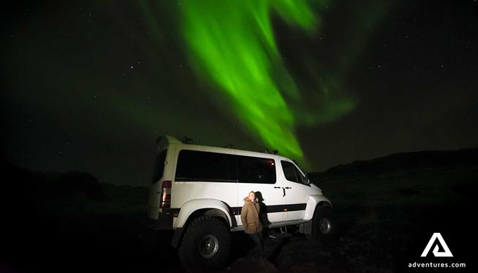 woman watching northern lights near a super jeep