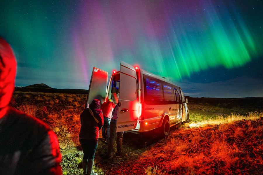 Tourists climbing up to Arctic Adventures tour bus during bright show of northern lights in Iceland.