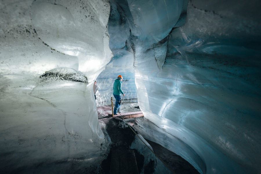 Interior of the Katla Ice Cave glowing with deep blue ice walls, layered with black volcanic ash, creating a striking contrast in the natural glacial tunnel.