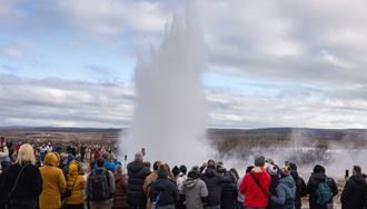 Crowd of people standing around geysir erupting in geothermal area of iceland