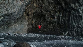 Man In A Cave On A Black Sand Beach In Iceland with basalt columns