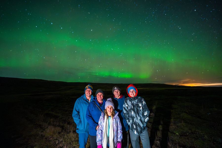 Family posing for photograph in late evening standing underneath starry sky with northern lights.