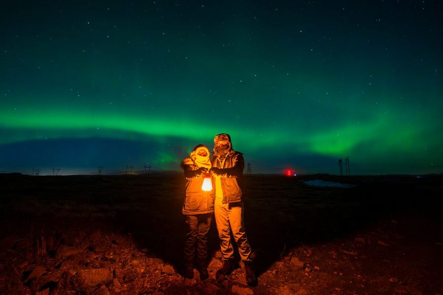 A Pair Holding A Lantern Standing Under Northern Lights In Iceland
