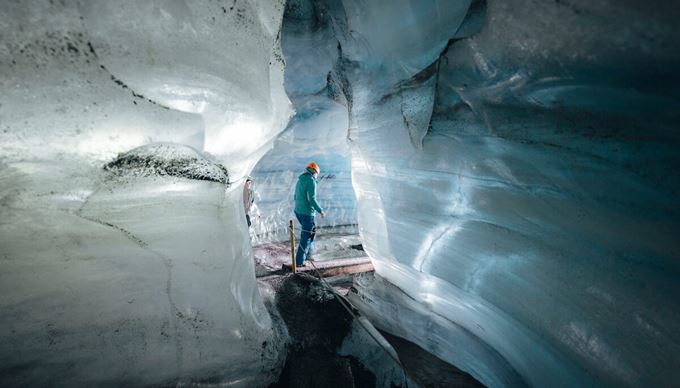 Interior of the Katla Ice Cave glowing with deep blue ice walls, layered with black volcanic ash, creating a striking contrast in the natural glacial tunnel.