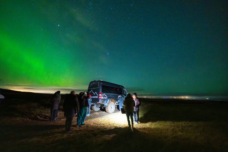 Small group tour of northern lights, group standing next to grey super jeep enjoying the green light show.