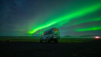 Adventures super jeep driving underneath bright green aurora borealis in Iceland.
