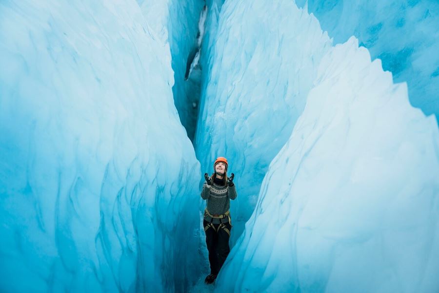 Tourist standing in between huge blue ice crevasse at Vatnajokull.